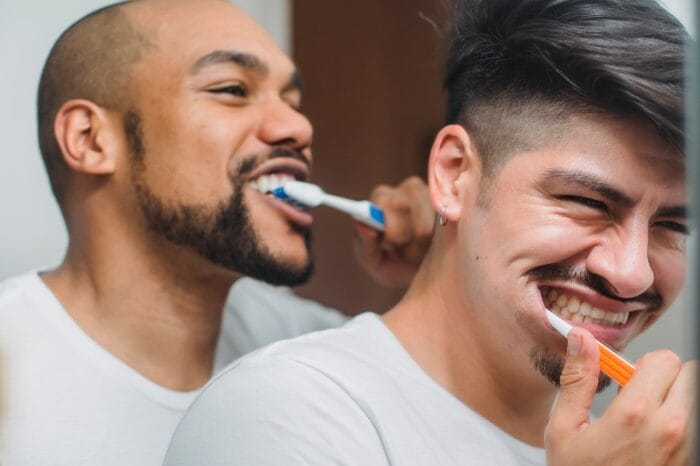 men brushing their teeth in the mirror