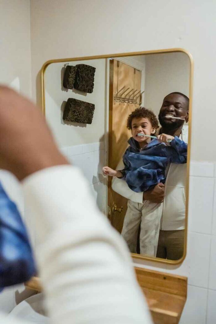 Bathroom mirror reflection of a father holding his young son while they brush their teeth together