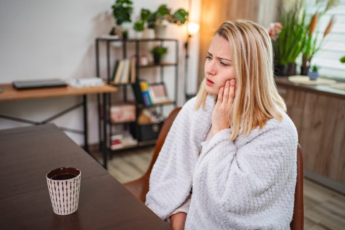 Woman holding cheek in pain while waiting for emergency dentist